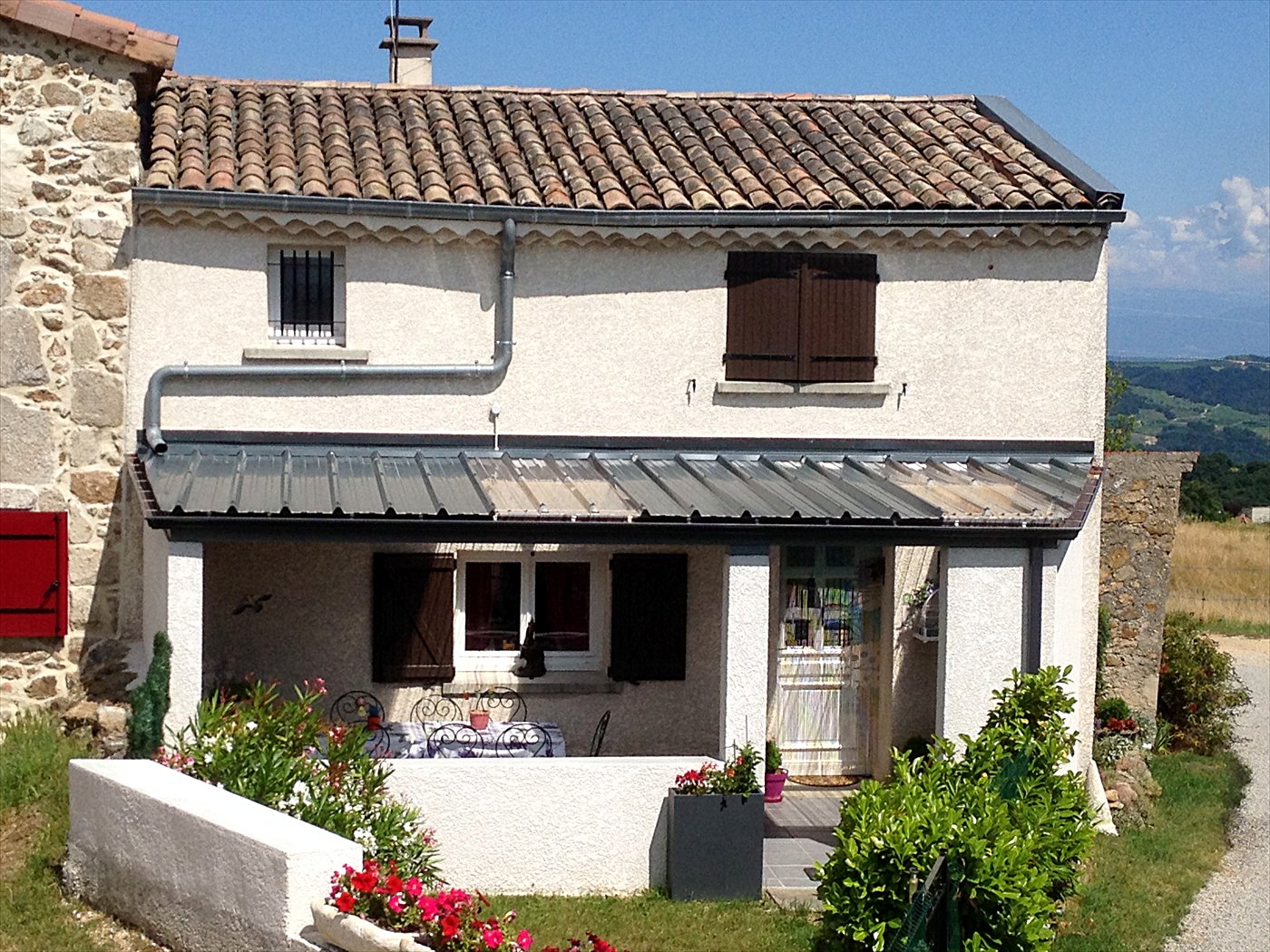 Maison en pierre avec un auvent en bac acier gris sur charpente bois devant la porte d&rsquo;entrée