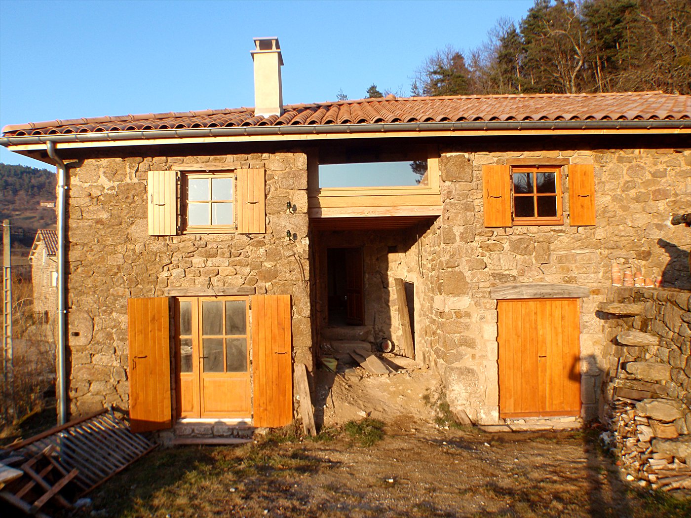 Maison de pierre rénovée avec fenêtres, porte-fenêtre, volets et porte de grange en bois