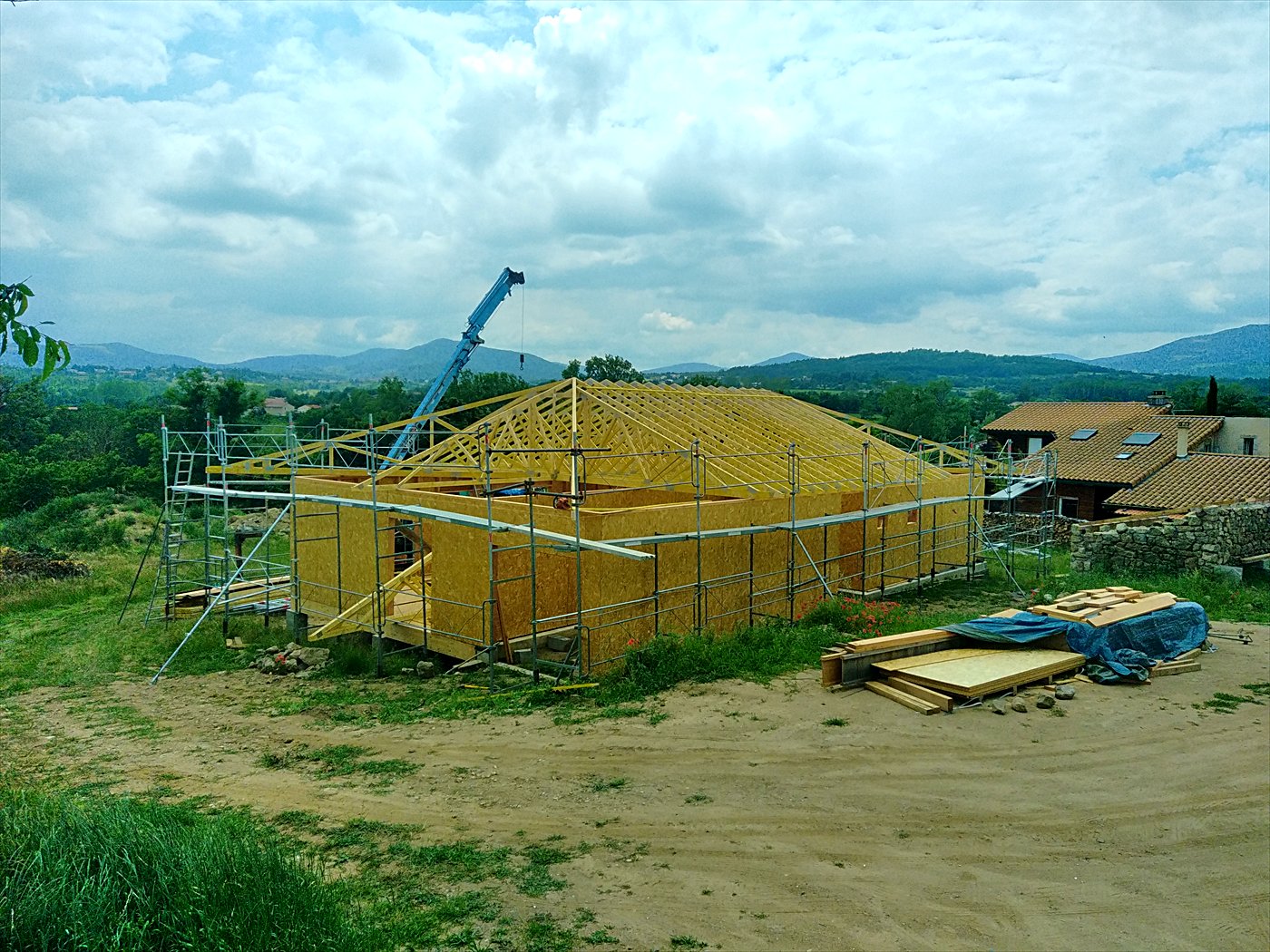 Maison à ossature bois en construction avec sa charpente en cours de pose, échafaudage et grue
