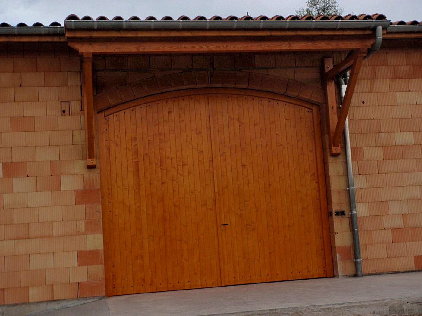 Porte de grange cintrée en bois sous un auvent de charpente